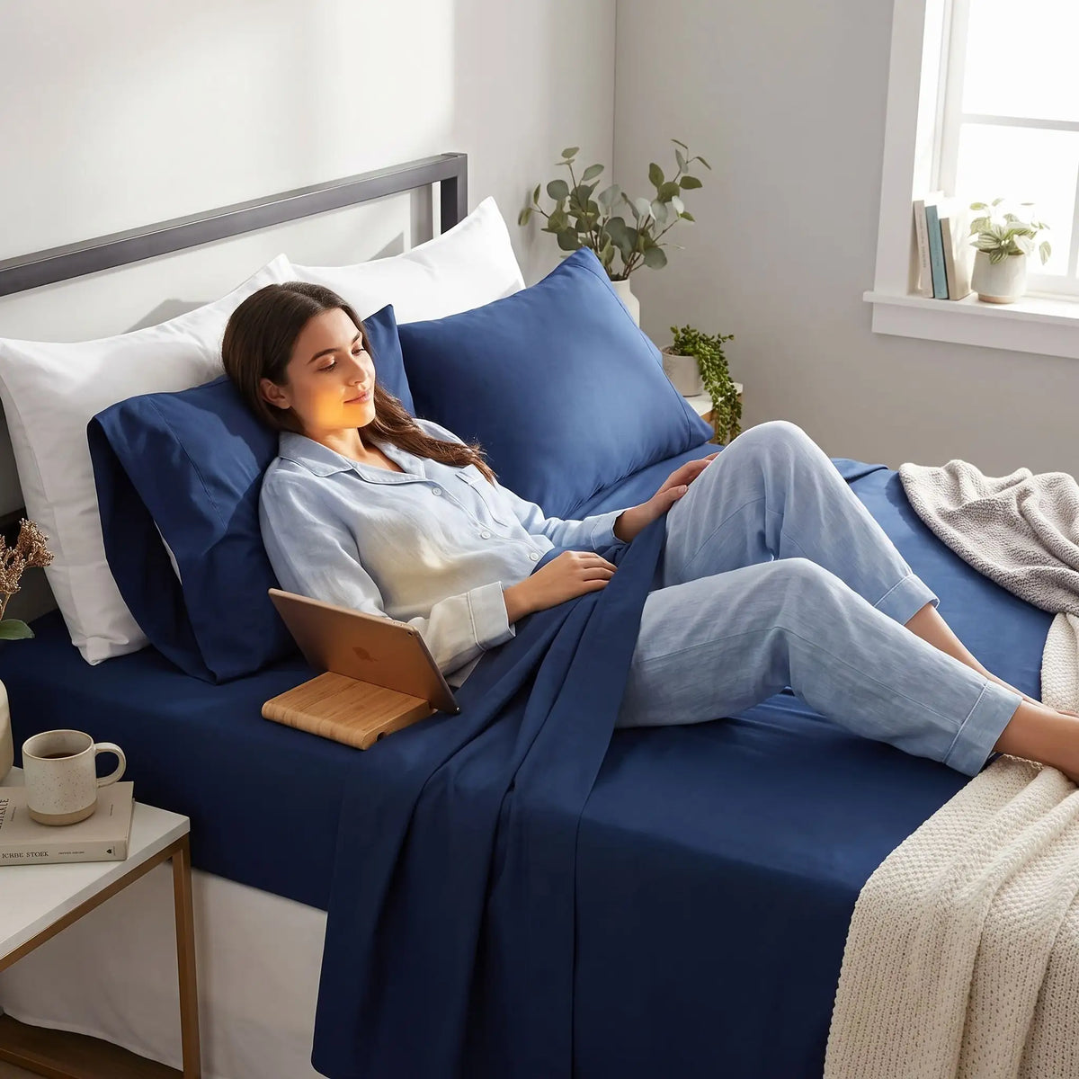 Femme couchée avec tablette sur dos sur draps doux bleu marine