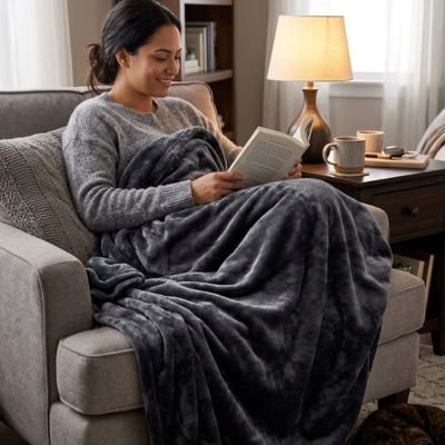 Femme souriante avec livre dans fauteuil sous couverture grise