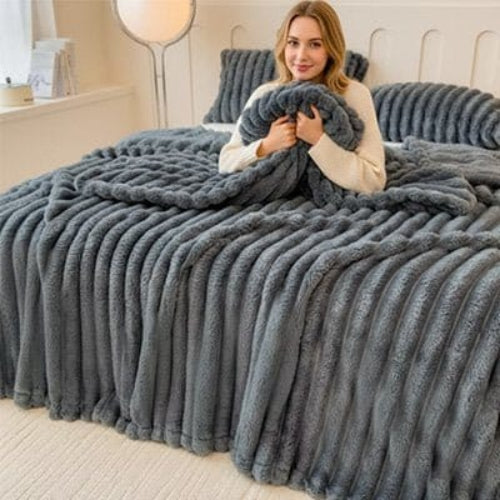 Femme sur lit sourit sous couverture grise