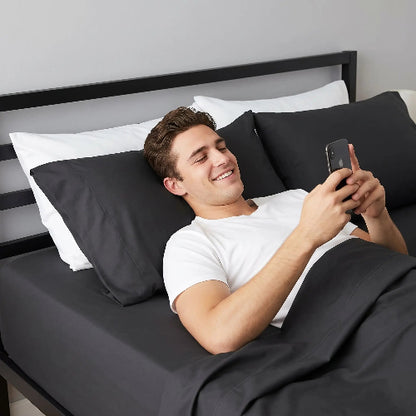 Homme souriant avec téléphone sur dos sur draps doux noirs 